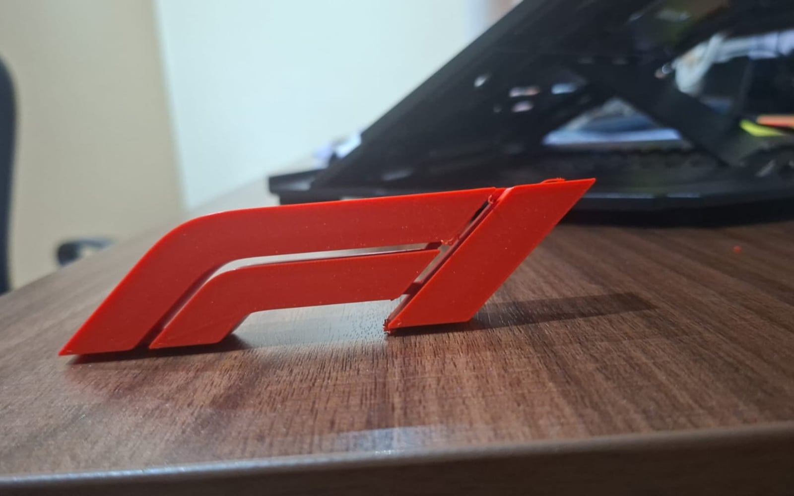 A red 3D-printed Formula 1 piece standing on a wooden desk.